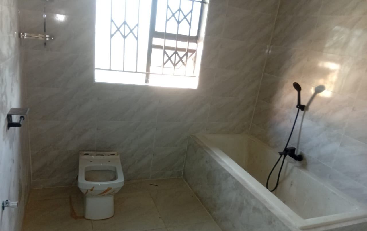 Built-in bath with black shower set and a close-coupled WC in a fully tiled bathroom