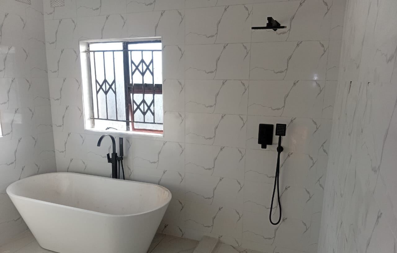 Freestanding bath and matt black floor-mounted mixer beside a walk-in shower in white marble tiling